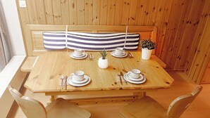 Una mesa de comedor de madera dispuesta con platos, tazas y cubiertos blancos, acompañada por dos sillas de madera.