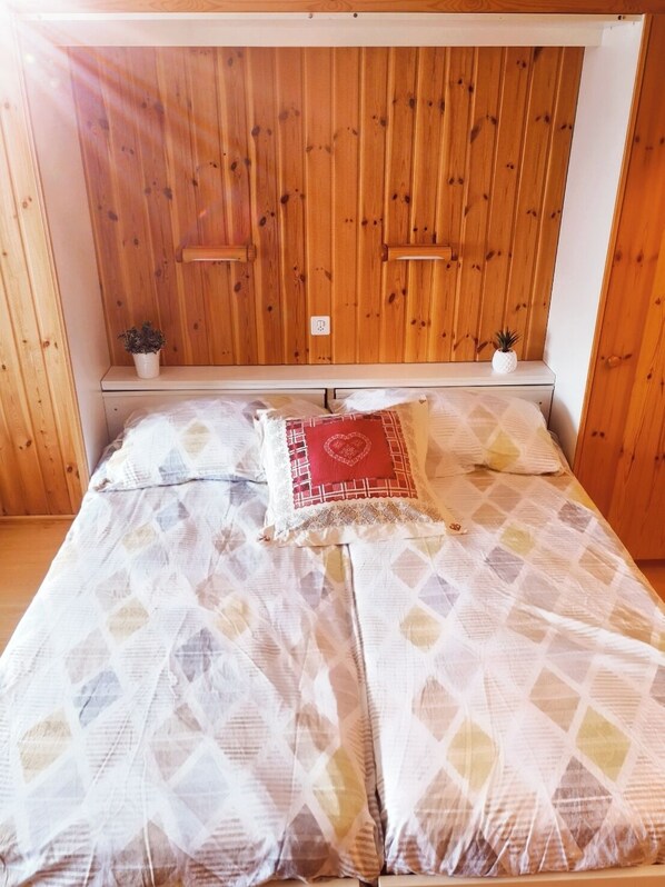 A wooden-paneled room with a bed featuring patterned bedding and a decorative pillow. - Superbe appartement au centre de Nendaz (Nendaz)