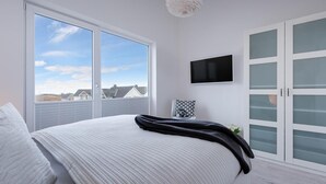 A bedroom with a large window, a bed with a striped blanket, a TV on the wall, and a wardrobe with frosted glass doors. - Nice apartment in Olpenitz with sauna (Olpenitz)