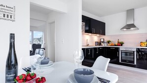 A modern kitchen with black cabinets, stainless steel appliances, and a white dining area with a bottle of wine, strawberries, and a bowl of fruit. - Nice apartment in Olpenitz with sauna (Olpenitz)