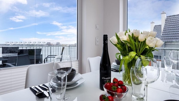 A dining table with a bottle of wine, a bowl of strawberries, and a vase of white flowers. - Nice apartment in Olpenitz with sauna (Olpenitz)