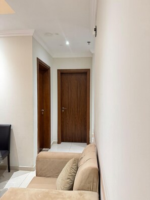 A hallway with two wooden doors, a beige sofa, and a small table with a chair.