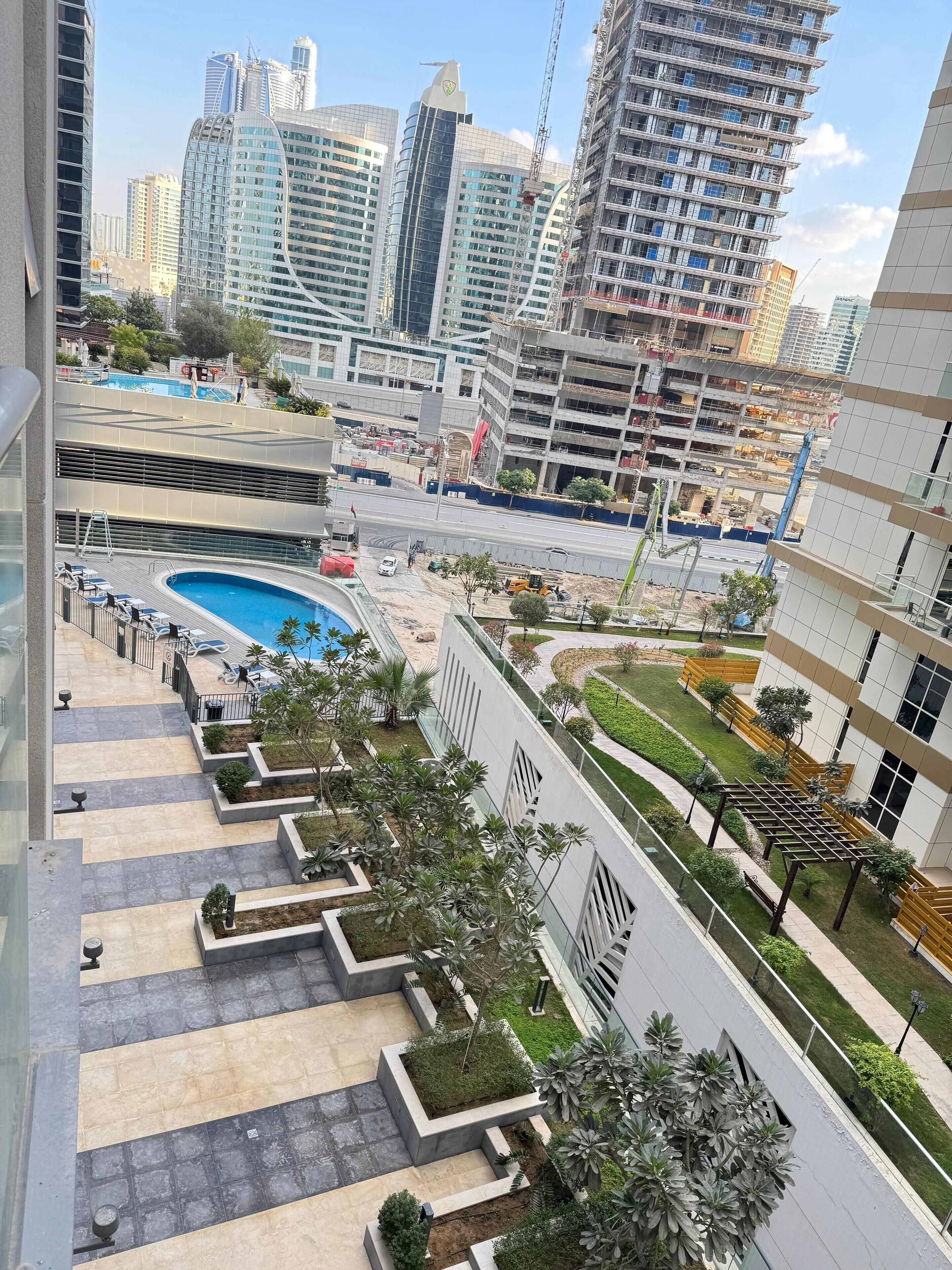 Un edificio residencial moderno con piscina en la azotea, jardines ajardinados y vistas del horizonte de la ciudad.