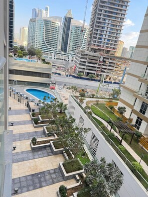 A modern residential building with a rooftop swimming pool, landscaped gardens, and a view of the city skyline.