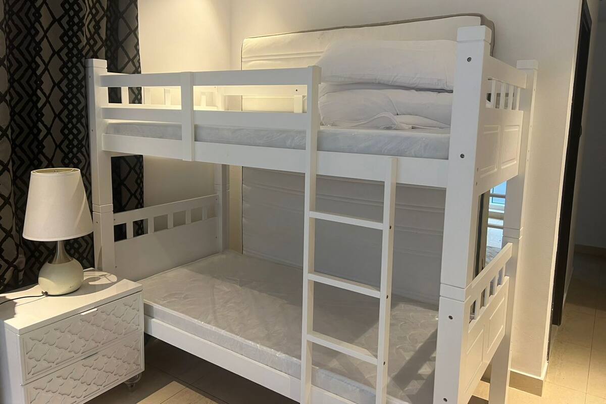 A bunk bed with a nightstand and lamp, a patterned curtain, and a tiled floor.
