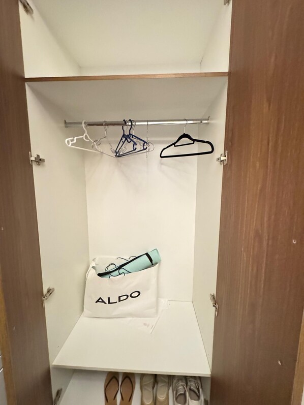 Un armario con una barra para colgar, una bolsa blanca de almacenamiento con la etiqueta "ALDO" y un par de zapatos en la parte inferior.