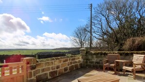 A patio with stone walls, wooden chairs, and a table. - Smugglers Rock House (Ravenscar, near Robin Hoods Bay)