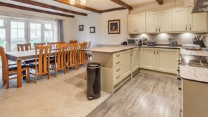 A modern kitchen with wooden beams, a dining area with a table and chairs, and a view of the outdoors through large windows. - Smugglers Rock House (Ravenscar, near Robin Hoods Bay)