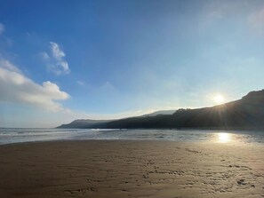Une plage où l’on peut voir des empreintes dans le sable, un ciel dégagé et le soleil se couchant sur l’eau.