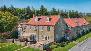 A stone building with a red-tiled roof, multiple windows, and a well-maintained lawn. - Smugglers Rock House (Ravenscar, near Robin Hoods Bay)