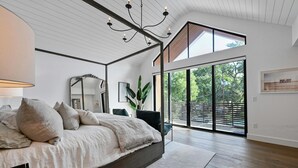 A modern bedroom with a large bed, a chandelier, and a view of the outdoors through large windows. - Luxe Home in Iconic Zilker/ Barton Springs neighborhood- POOL (Austin)