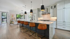A modern kitchen with white cabinets, a large island with bar stools, pendant lighting, and a view of the outdoors. - Luxe Home in Iconic Zilker/ Barton Springs neighborhood- POOL (Austin)