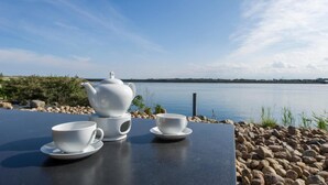 A table with a teapot and two cups set on a lakeside table, surrounded by rocks. - Yachtblick auf der Ostsee (Olpenitz)
