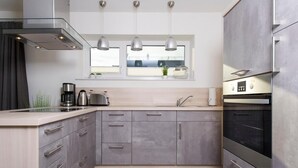 A modern kitchen with grey cabinets, stainless steel appliances, and pendant lighting. - Yachtblick auf der Ostsee (Olpenitz)