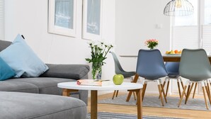 Una sala moderna con un sofá gris, una mesita redonda con un libro y una manzana verde, y un jarrón con flores blancas.