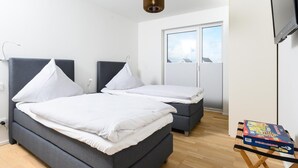 Un dormitorio con dos camas, una mesita con un juego de mesa y una ventana con persianas.