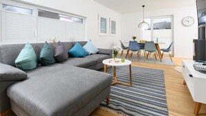 Una sala de estar moderna con un sofá seccional gris, una mesita blanca y un comedor con sillas y una mesa.