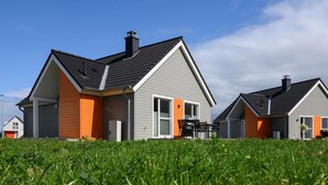 Dos casas modernas con revestimiento gris y naranja, techos negros y un césped.