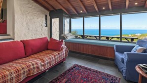 Una stanza con soffitto in legno, un divano rosso, un divano blu e vista mare.