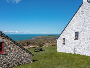 Un edifici de pedra amb una porta vermella, un edifici blanc amb finestres i vista al mar.