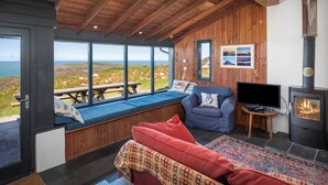 Una stanza accogliente con soffitto in legno, un camino, un divano, una TV e vista sul paesaggio.