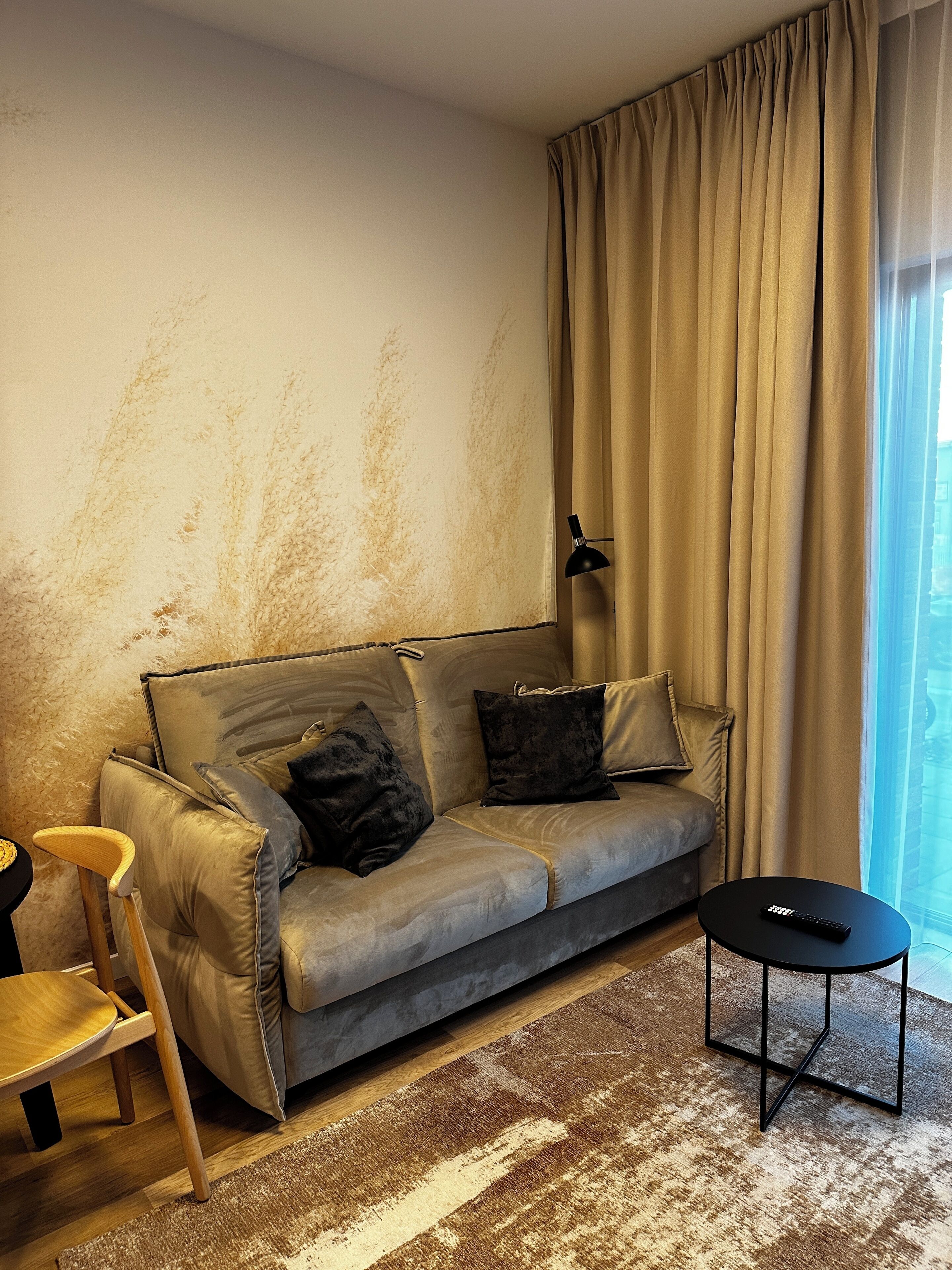 A living room with a sofa, a small table, a lamp, and a view through a window.