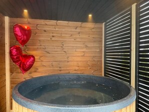 A hot tub in a wooden cabin with a wooden wall and a window with horizontal blinds.