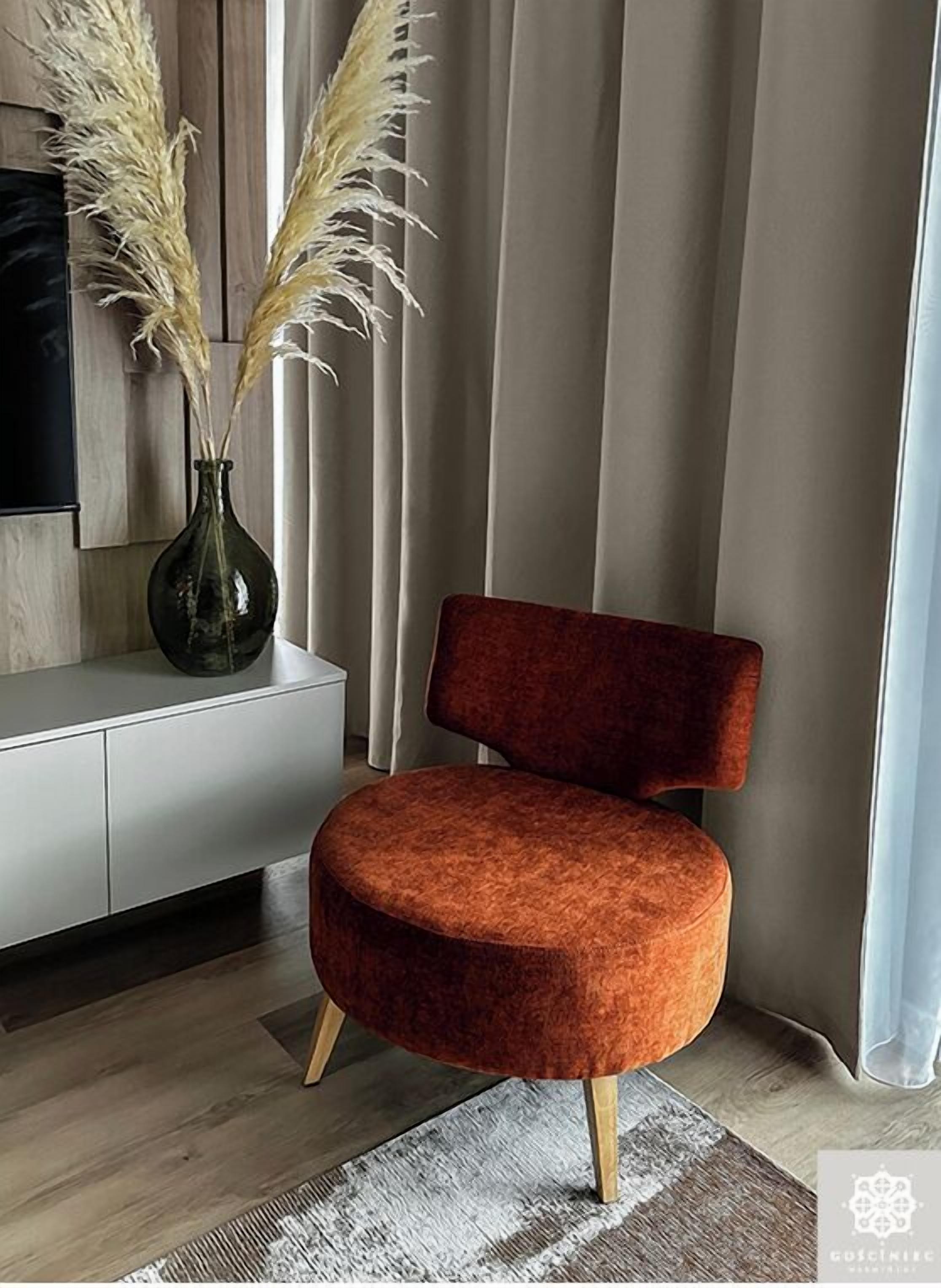 A modern living room with a round, orange upholstered chair, a wooden cabinet, and a vase with pampas grass.