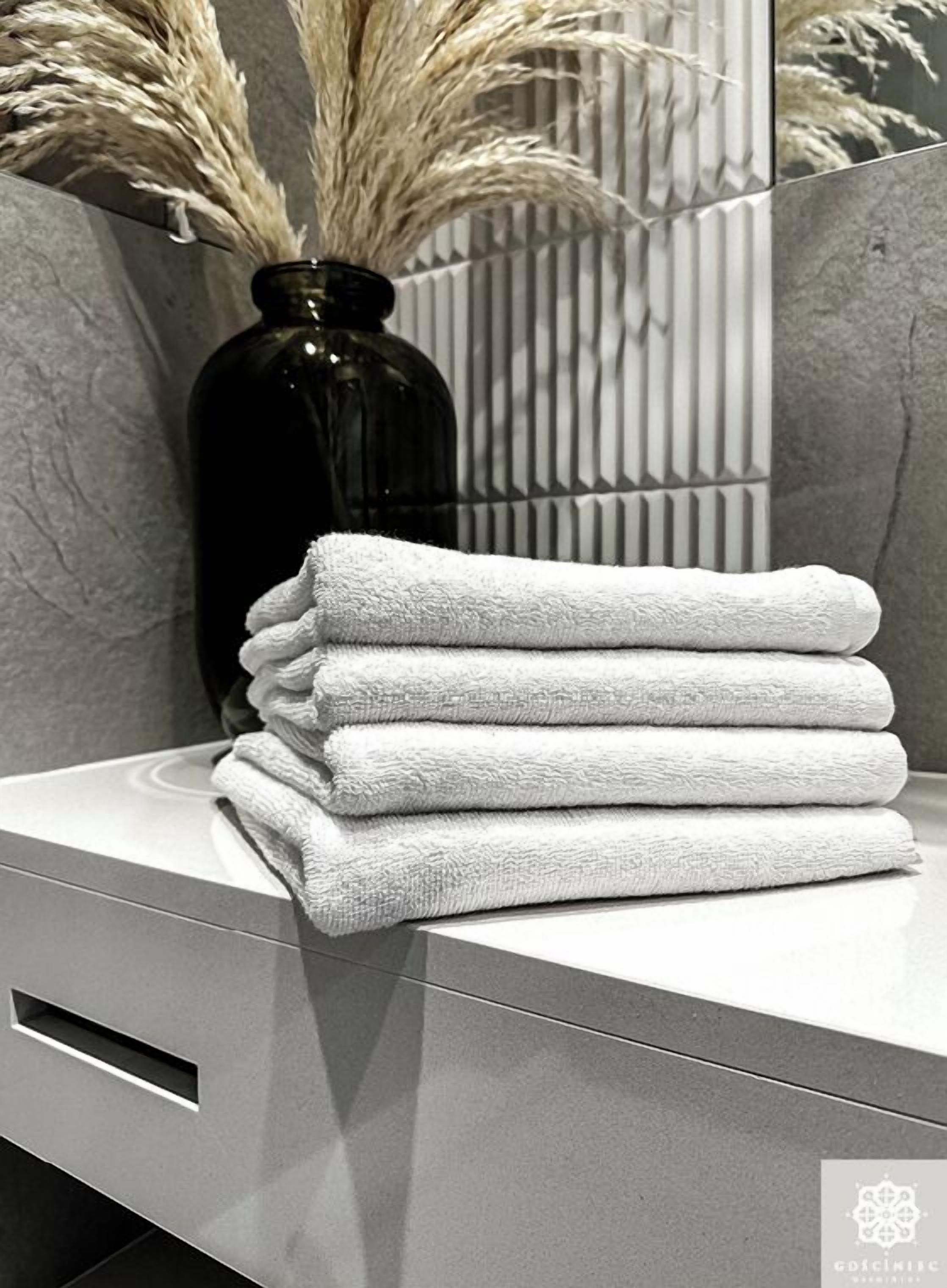 A stack of white towels on a modern bathroom counter with a dark vase and pampas grass.