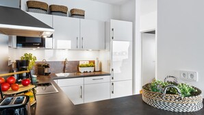 Una cocina moderna con armarios blancos, un extractor Bosch, un fregadero y un horno empotrado. Hay cestas en la encimera y una cesta tejida con flores en el suelo.