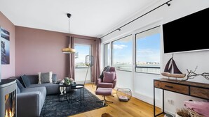 Una sala de estar moderna con sofá, una butaca, una mesa de centro, chimenea y un amplio ventanal con vistas a la ciudad.