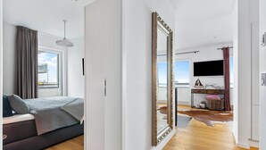 Un dormitorio moderno con un espejo grande, una cama con colcha gris, suelo de madera y vistas al exterior.