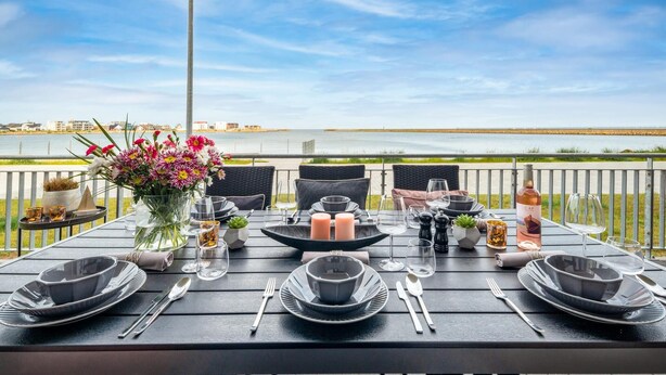 Una mesa para dos con vista al mar, un arreglo floral y una botella de vino.
