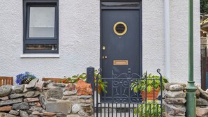 Una casa con puerta azul oscuro, una ventana y un muro de piedra.