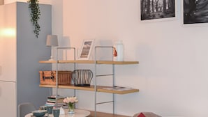 Una sala de estar moderna con una mesa redonda, sillas grises, un sofá con cojines rojos, una estantería y un cuadro enmarcado en la pared.