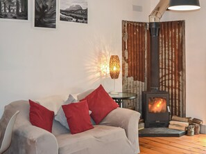 A cozy living room with a sofa, a table with a lamp, a rustic wall, and a wood-burning stove. - 1 bedroom accommodation in Inverness (Inverness)