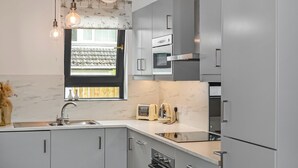 Una cocina moderna con armarios grises, horno empotrado, microondas y una ventana con vista a un jardín.