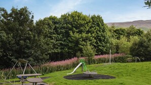 Un parque infantil con un tobogán y columpios, rodeado de exuberante vegetación y plantas en flor.