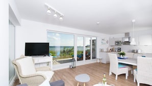 Una sala de estar moderna con televisor, mobiliario de mimbre, una zona de comedor y una cocina.