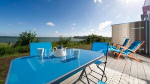 Una mesa con vista al mar, un edificio pequeño y dos sillones de descanso.