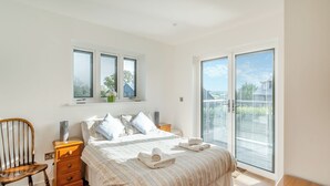 A bedroom with a bed, a chair, a nightstand, a window, and a sliding glass door leading to a balcony. - Fair Isle Holiday Cottages - Fisher (Near Newport)
