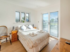 A bedroom with a bed, a chair, a nightstand, a window, and a sliding glass door leading to a balcony. - Fair Isle Holiday Cottages - Fisher (Near Newport)