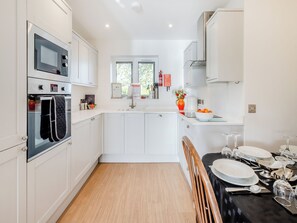 Una cocina moderna con armarios blancos, horno empotrado, ventana y comedor dispuesto para cuatro comensales.