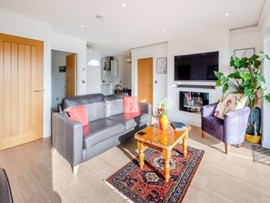 Una sala de estar moderna con un sofá gris, una mesa de centro de madera, una alfombra estampada, un televisor y una chimenea.