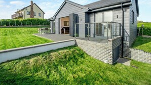 A modern house with a patio, a brick wall, and a large glass door. - Fair Isle Holiday Cottages - Fisher (Near Newport)