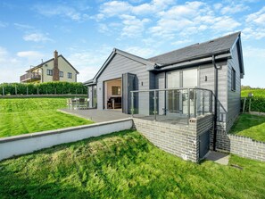 A modern house with a patio, a brick wall, and a large glass door. - Fair Isle Holiday Cottages - Fisher (Near Newport)