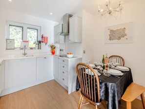 Een moderne keuken met witte kasten, een eethoek met een tafel gedekt voor vier personen, en een kroonluchter.