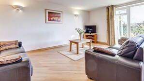 Un salon moderne avec un canapé, une table basse, un téléviseur posé sur un meuble en bois et un tableau accroché au mur.