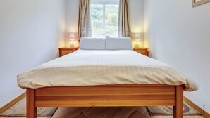 Une chambre à coucher avec un lit en bois, deux tables de chevet avec des lampes, une fenêtre avec des rideaux et un tableau au mur.