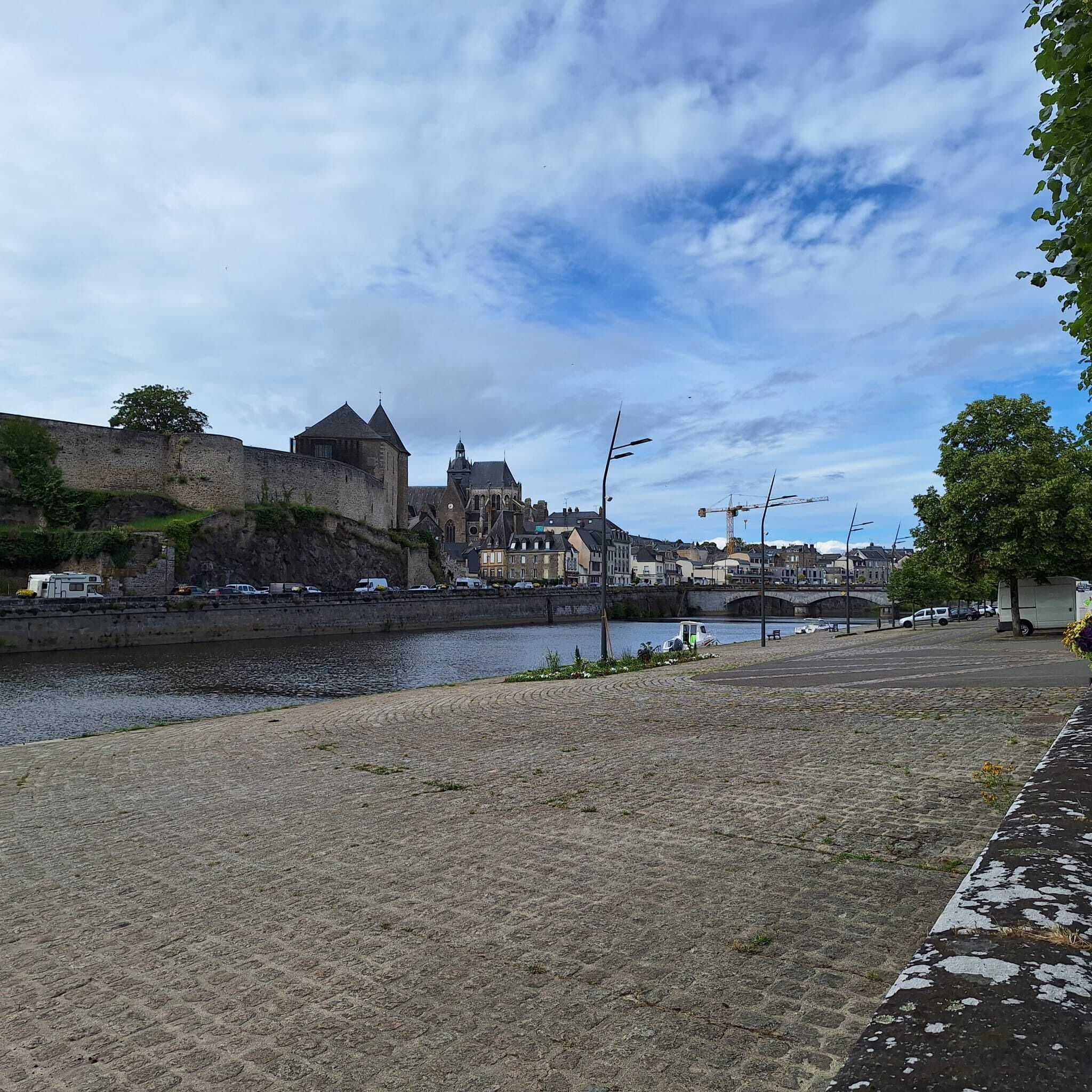 A riverside view with a historic building, a bridge, and a paved walkway.